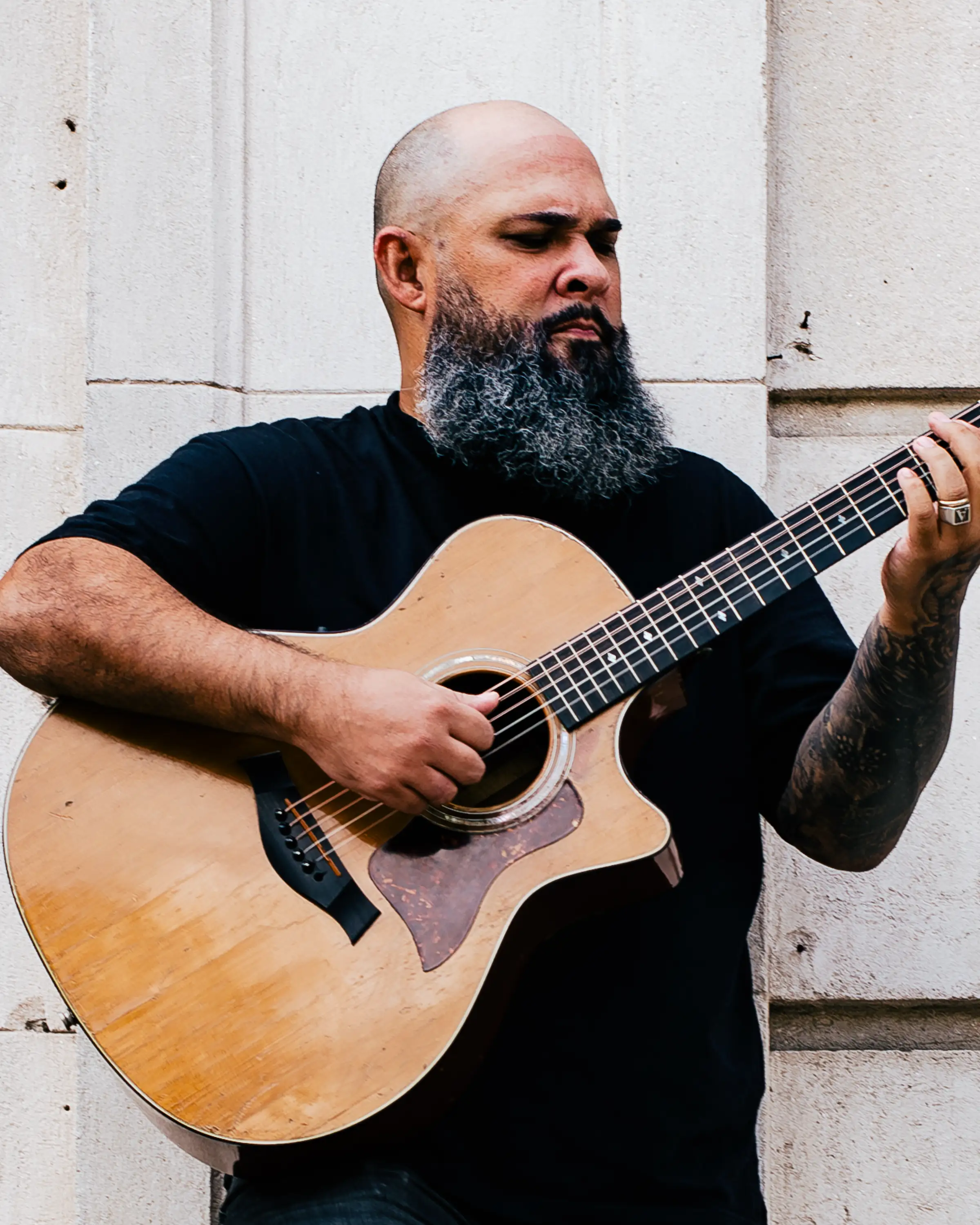 Vitor Teixeira tocando violão junto a uma parede de pedra