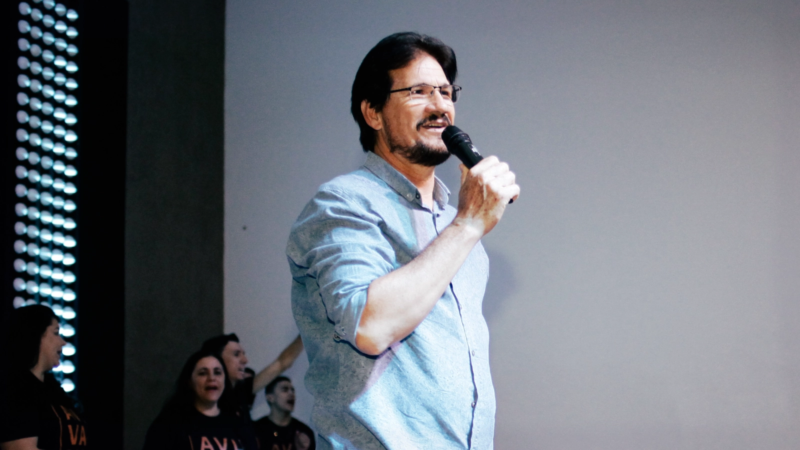Vocalista do Musical Formosa canta ao microfone durante um culto, com integrantes ao fundo